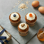 Three cupcakes with cream toppings on a gray surface with oats, honey and eggs.